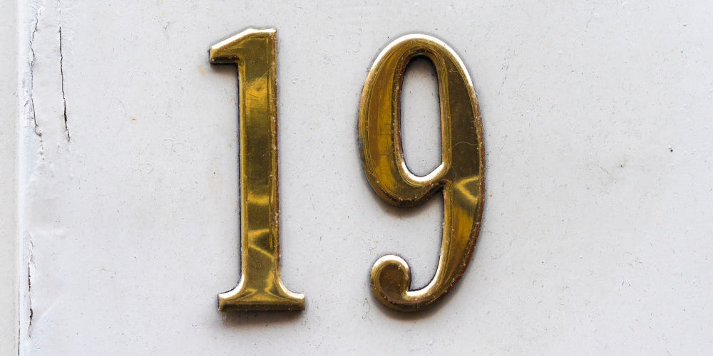 chiffre 19 doré en relief sur mur blanc symbolisant l'heure miroir 19h19 et la confiance en soi