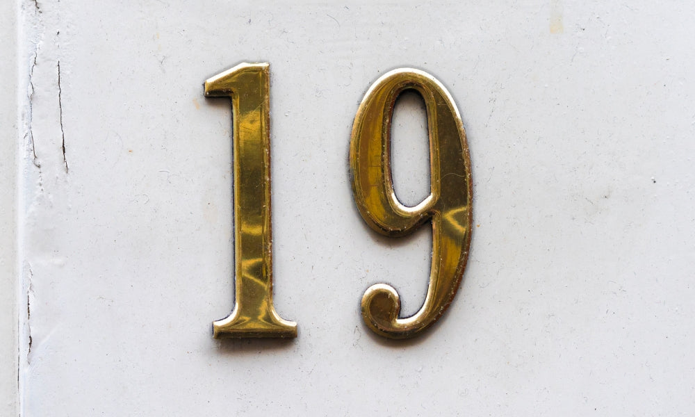chiffre 19 doré en relief sur mur blanc symbolisant l'heure miroir 19h19 et la confiance en soi